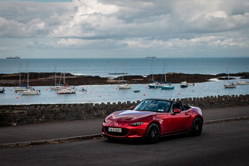 Red Mazda MX-5 convertible parked by a stone wall